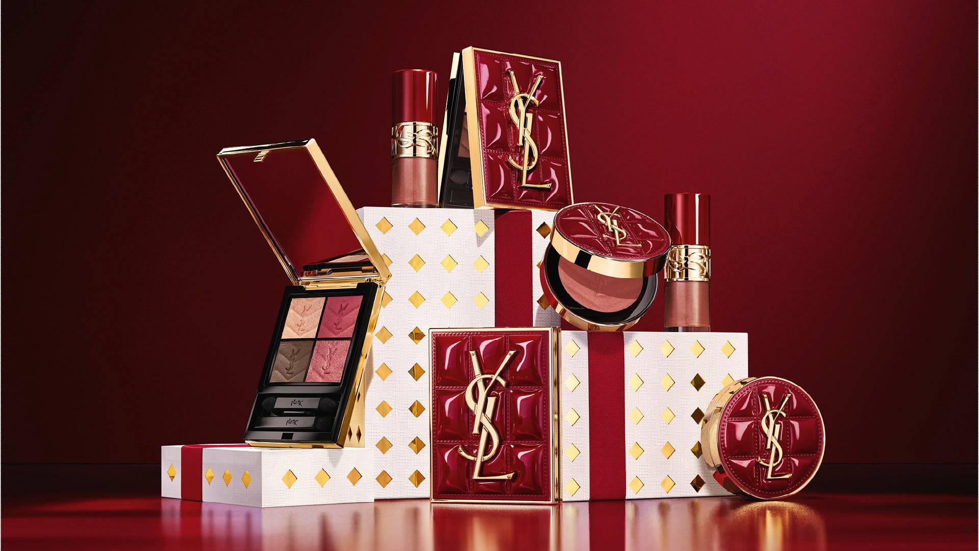YSL burgundy and gold holiday makeup displayed on white gift plinths against a dark burgundy background.