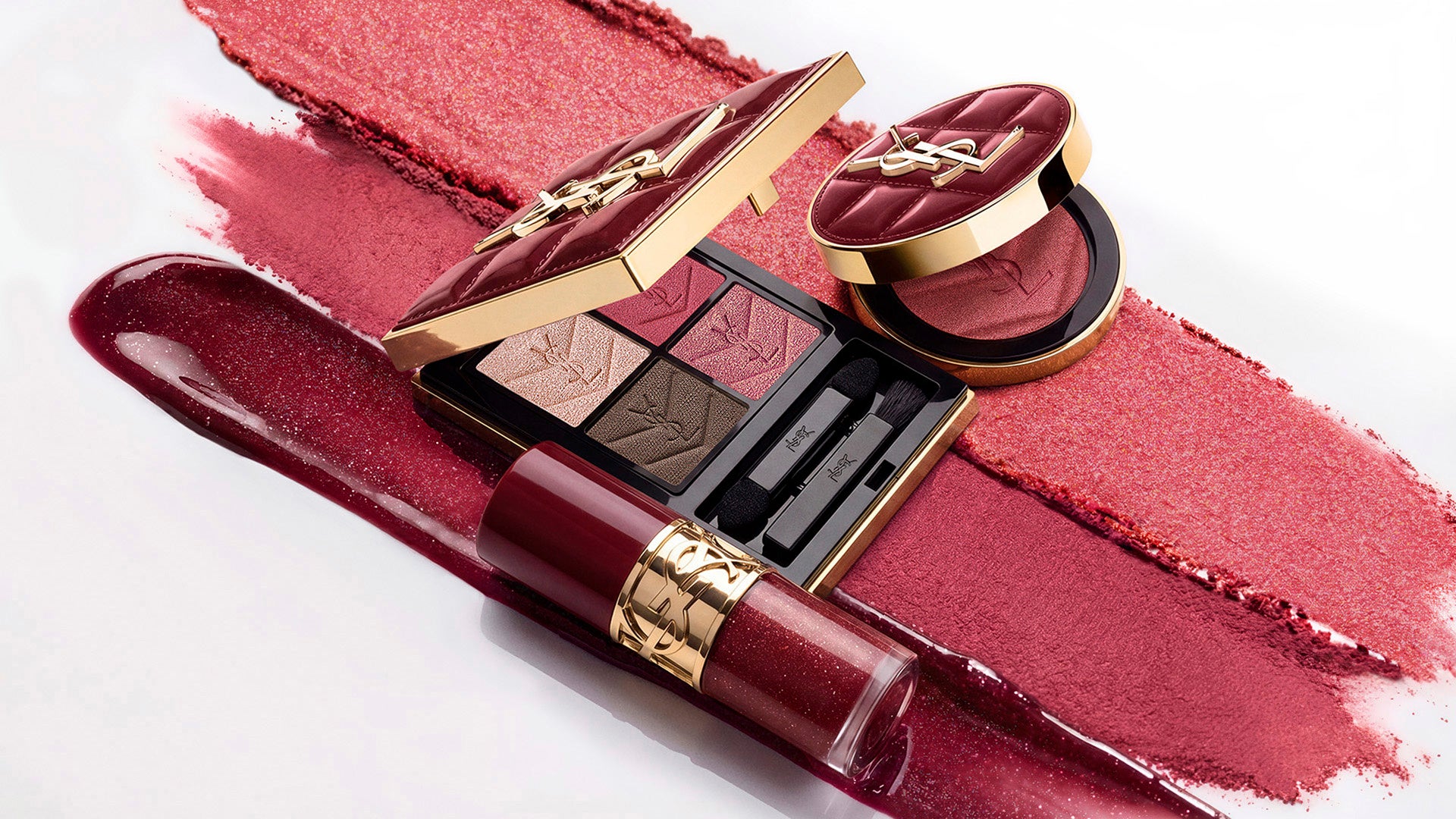 YSL burgundy holiday eyeshadow palette, blush and lip oil arranged over pink powder and burgundy gloss swatches.