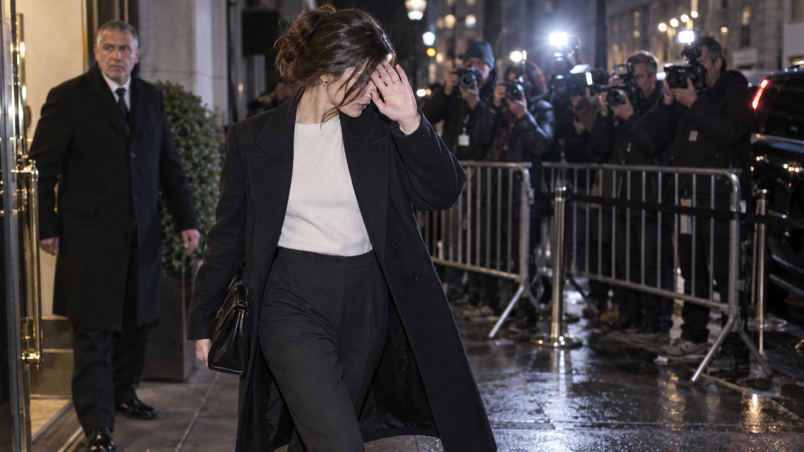 A woman shielding her face from cameras outside a building at night.